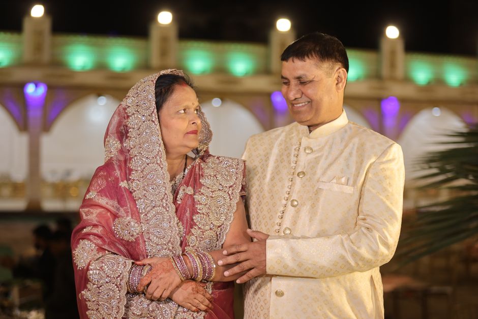 A smiling Indian couple elegantly dressed at a festive nighttime wedding event, celebrating joy and tradition.