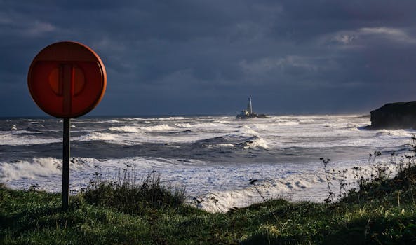 Waves crashing on a stormy coast with a distant lighthouse under a dark sky.