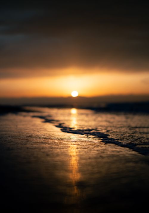 Free Peaceful sunset reflecting over gentle waves on a calm beach shore. Stock Photo
