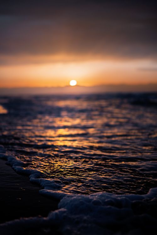 Free Serene sunset over the ocean with gentle waves and a warm glow reflecting on the water. Stock Photo