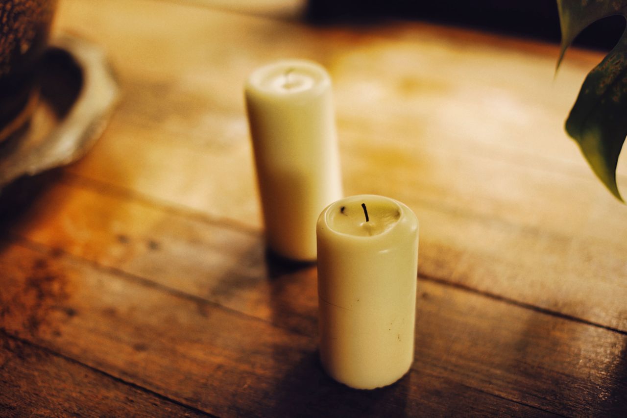 Two cream pillar candles on a wooden surface