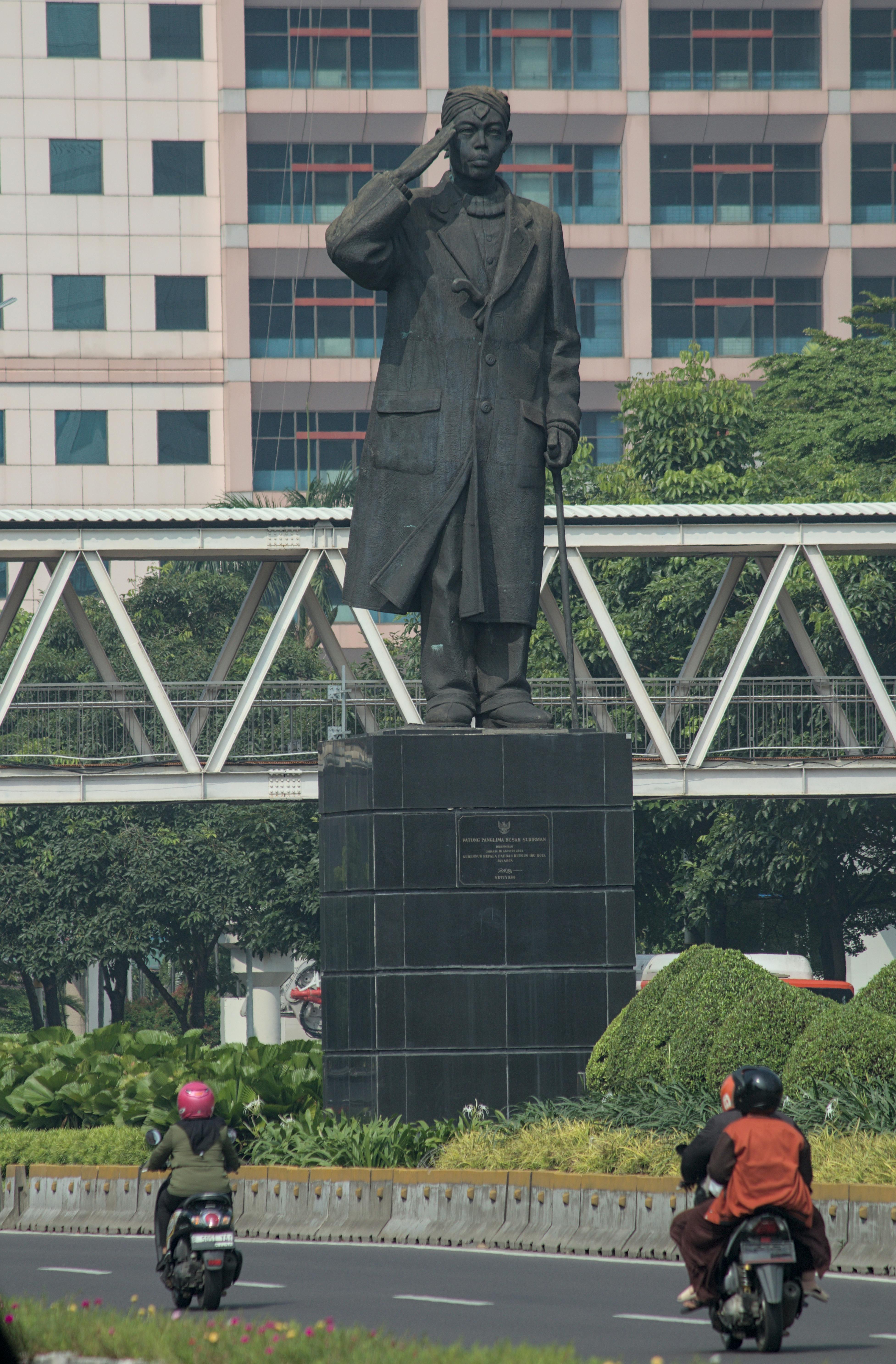 A statue of a notable figure in the city surrounded by busy streets, greenery, and buildings.