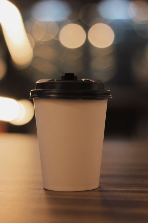Free Simple paper coffee cup on a table with soft bokeh lights in the background, providing a warm and cozy feel. Stock Photo