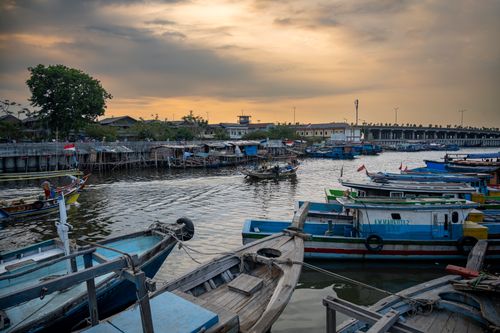 Free Peaceful scene at a Jakarta fishing village with colorful boats and a dramatic sunset sky. Stock Photo