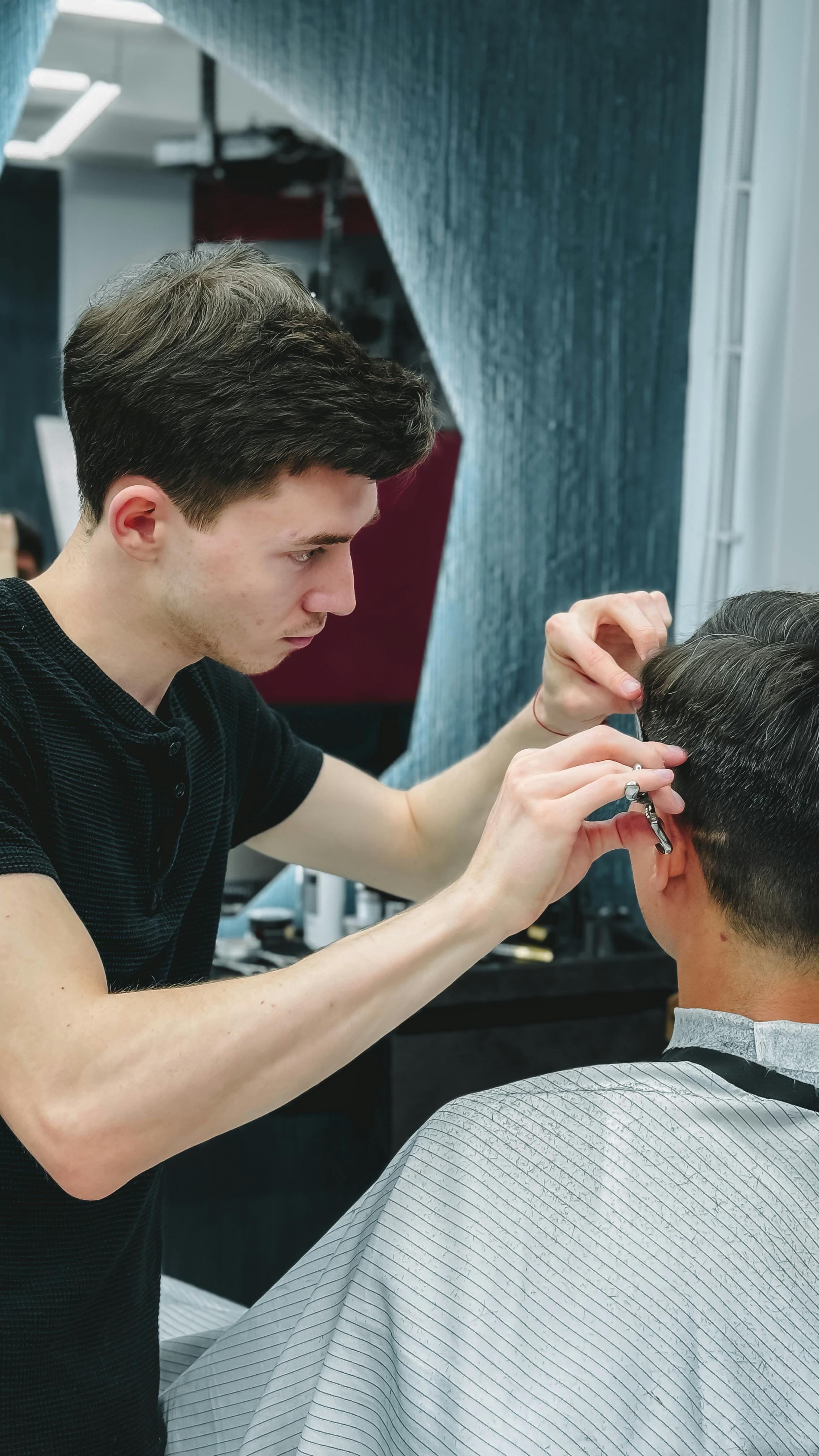 Barber focused on styling a client's hair with scissors in a contemporary salon setting.