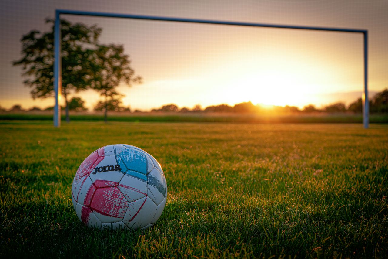 a soccer ball on a grassy field with a goal post beautifully lit by th