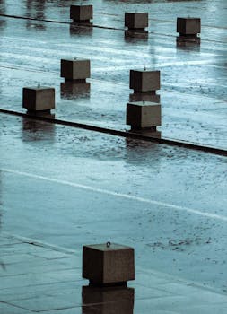 A rainy city street with concrete blocks reflecting on wet pavements.