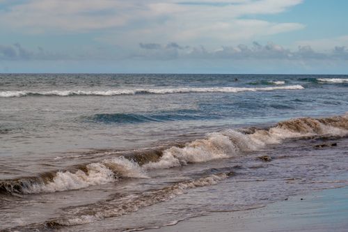 Free Calm ocean waves gently rolling onto a sandy shore under a cloudy sky. Stock Photo