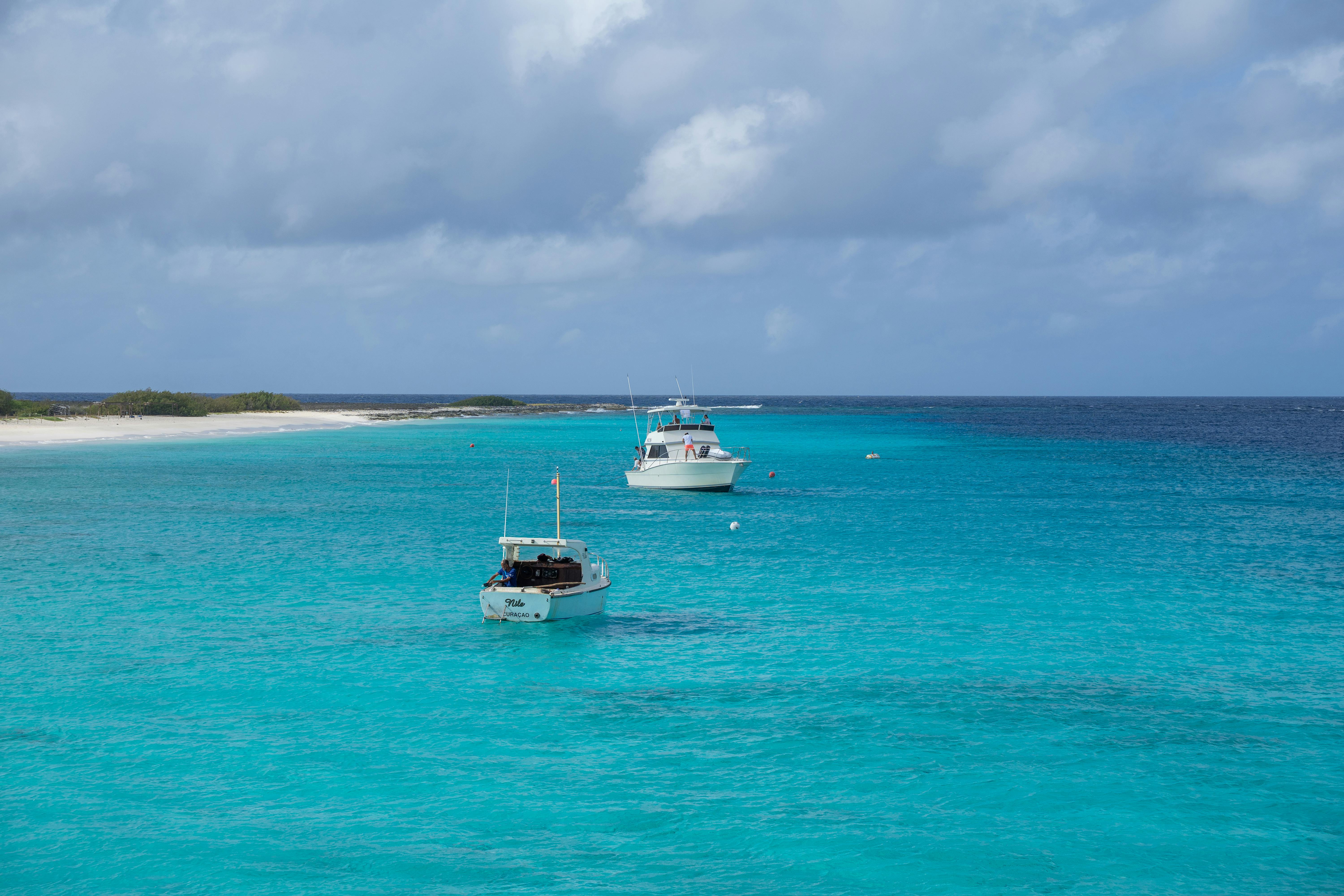 Two boats floating on clear turquoise ocean waters near a sandy beach in Curaçao.