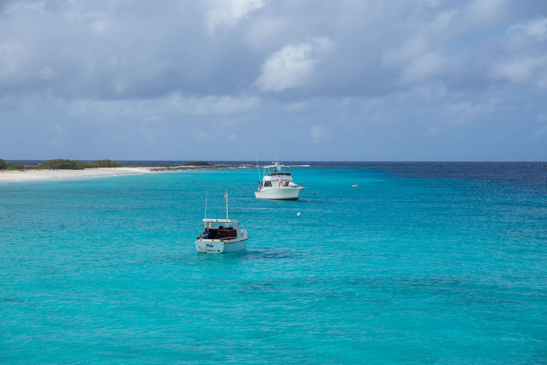 Two boats floating on clear turquoise ocean waters near a sandy beach in Curaçao.