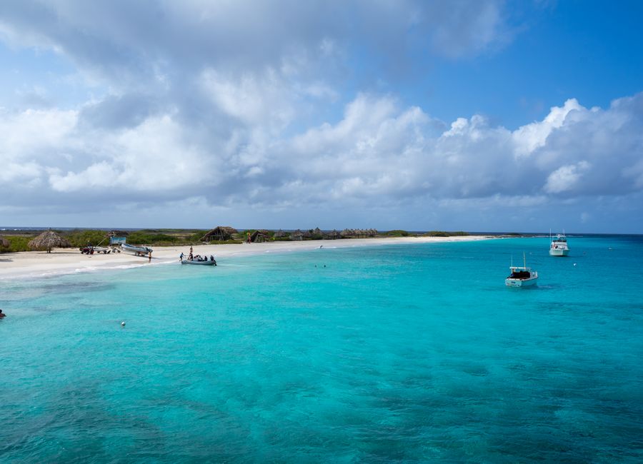 Experience the serene beauty of a Curaçao beach, with vibrant turquoise waters and scattered boats under a vast sky.