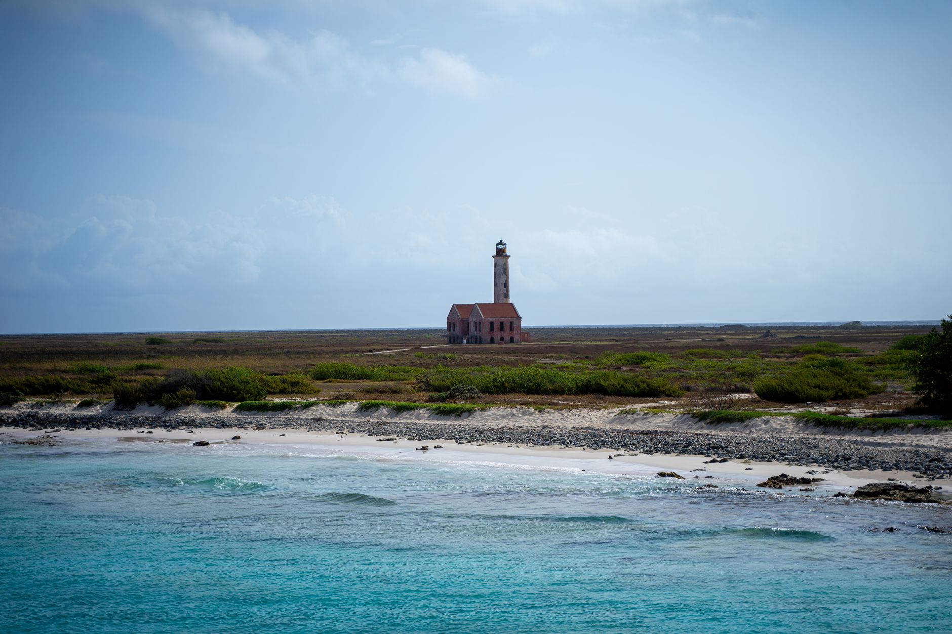 Scenic coastal landscape featuring the abandoned lighthouse of Klein Curaçao under a bright sky.