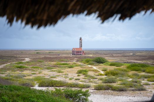 Une vue lointaine du phare historique de Klein Curaçao avec un paysage accidenté et un ciel en arrière-plan.