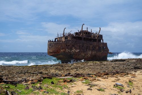Free A dramatic view of a rusted shipwreck on Curaçao's rocky shoreline under a clear blue sky. Stock Photo