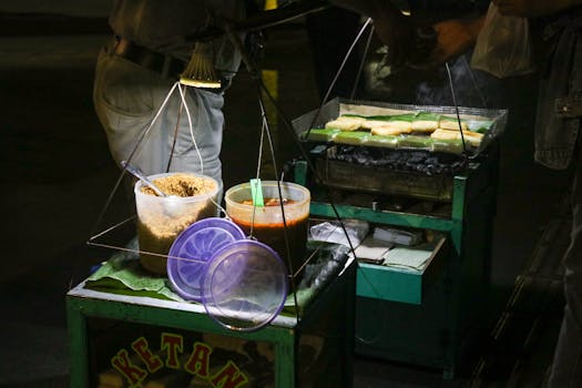 A vibrant street food scene at night featuring a vendor grilling ketan rice cakes in Indonesia.