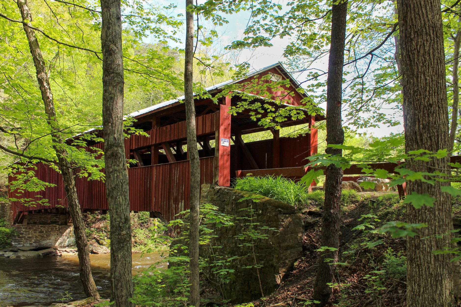 Most Photogenic Covered Bridges in Vermont 3 A picturesque red covered bridge in a lush springtime forest setting.