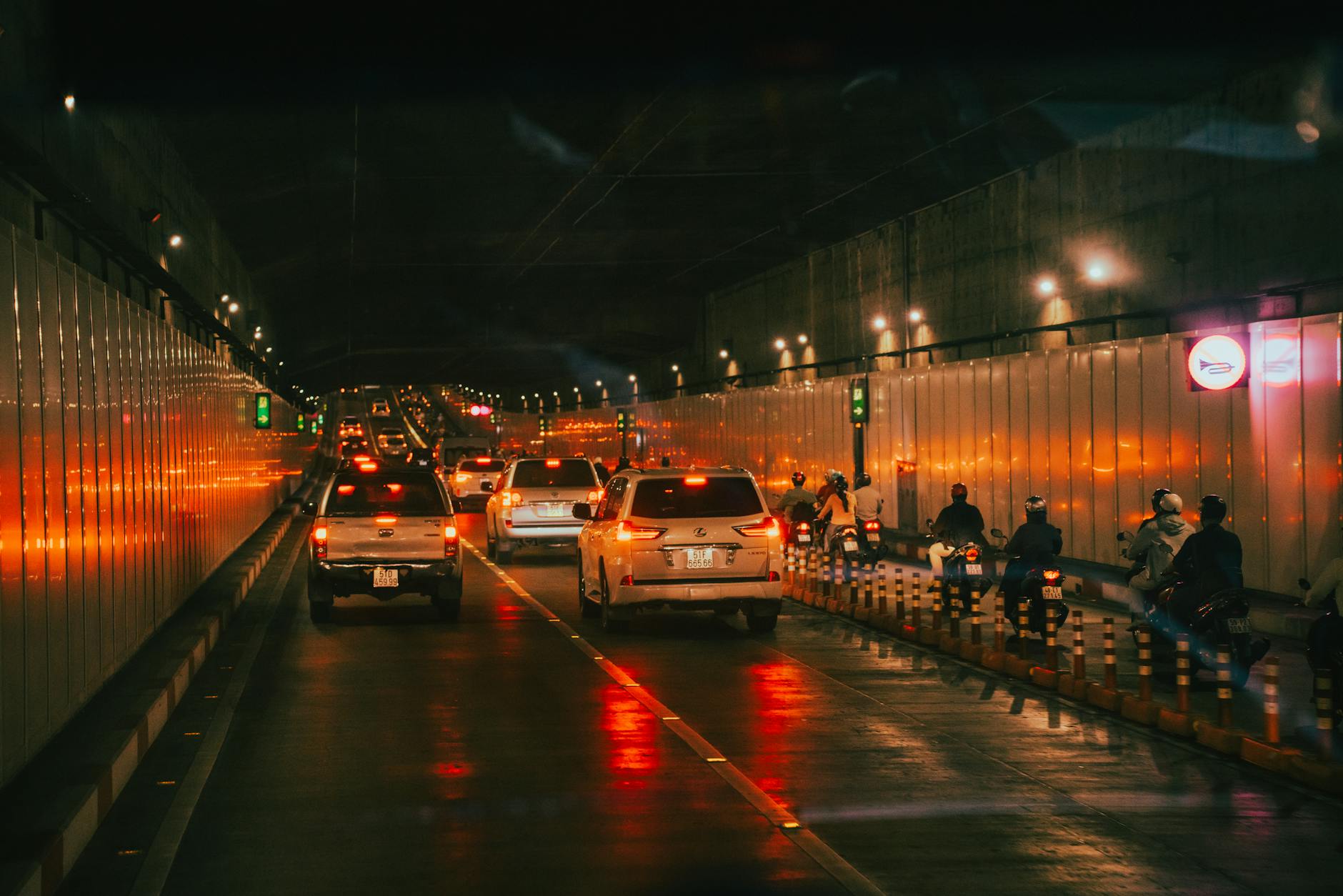 Dynamic scene in a Hồ Chí Minh City tunnel featuring cars and motorbikes under warm lights.