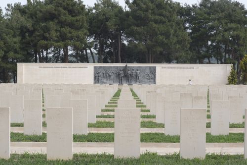 Free Serene military cemetery with aligned tombstones, a memorial wall, and lush trees. Stock Photo
