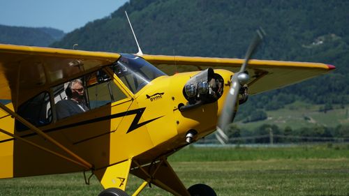 Free Close-up of a yellow vintage aircraft with a pilot outdoors, against a scenic mountain backdrop. Stock Photo