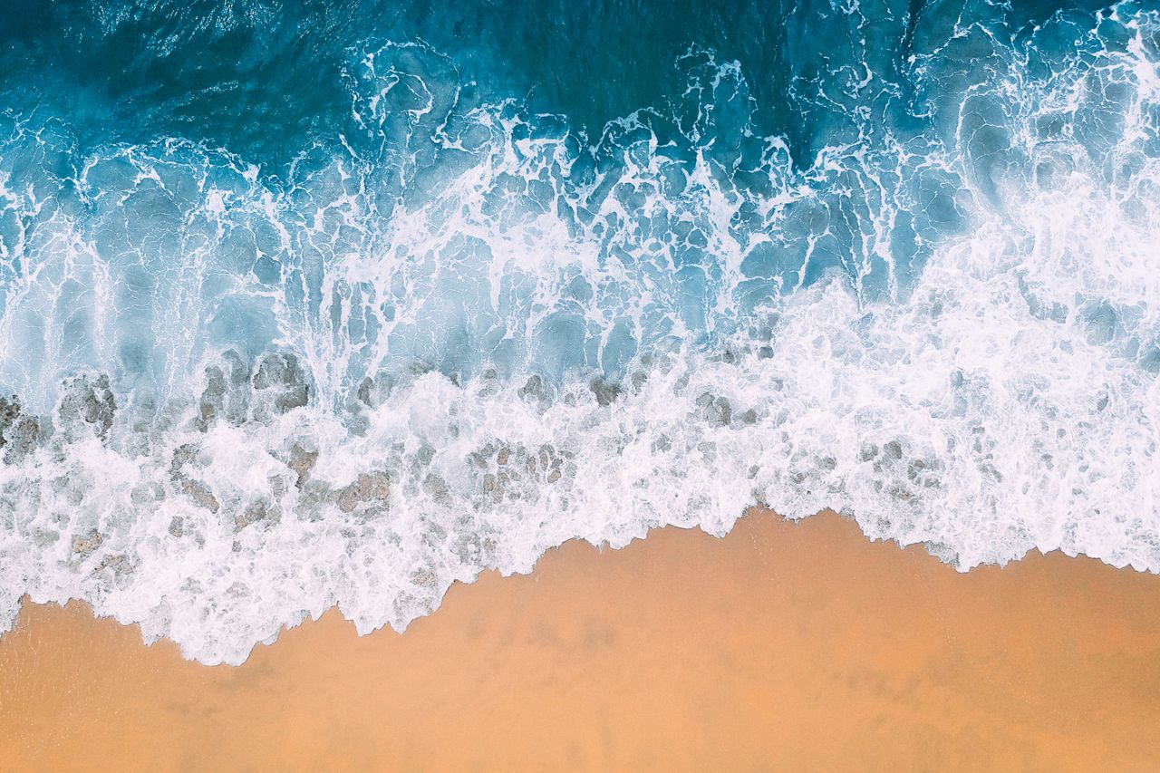 a breathtaking aerial shot capturing the waves crashing on a sandy bea