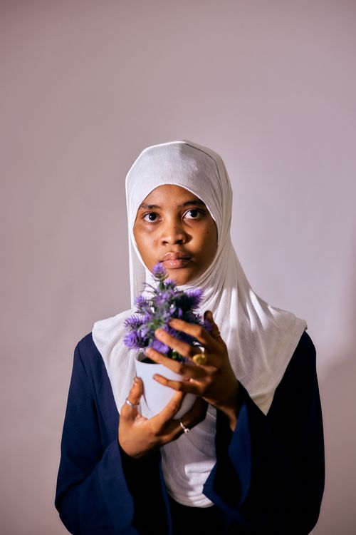 Free Portrait of a young woman in a hijab holding a purple flower bouquet against a neutral background. Stock Photo
