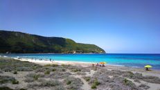 Vibrant turquoise waters and sandy beach with umbrellas and people under a clear blue sky.