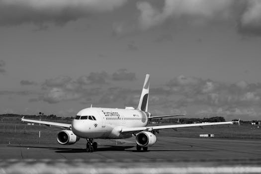Black and white photo of a commercial airplane on the runway with a cloudy sky backdrop.