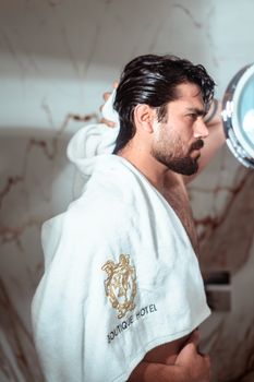 A man grooming himself in a luxury bathroom with a Boutique Hotel towel draped over his shoulder.