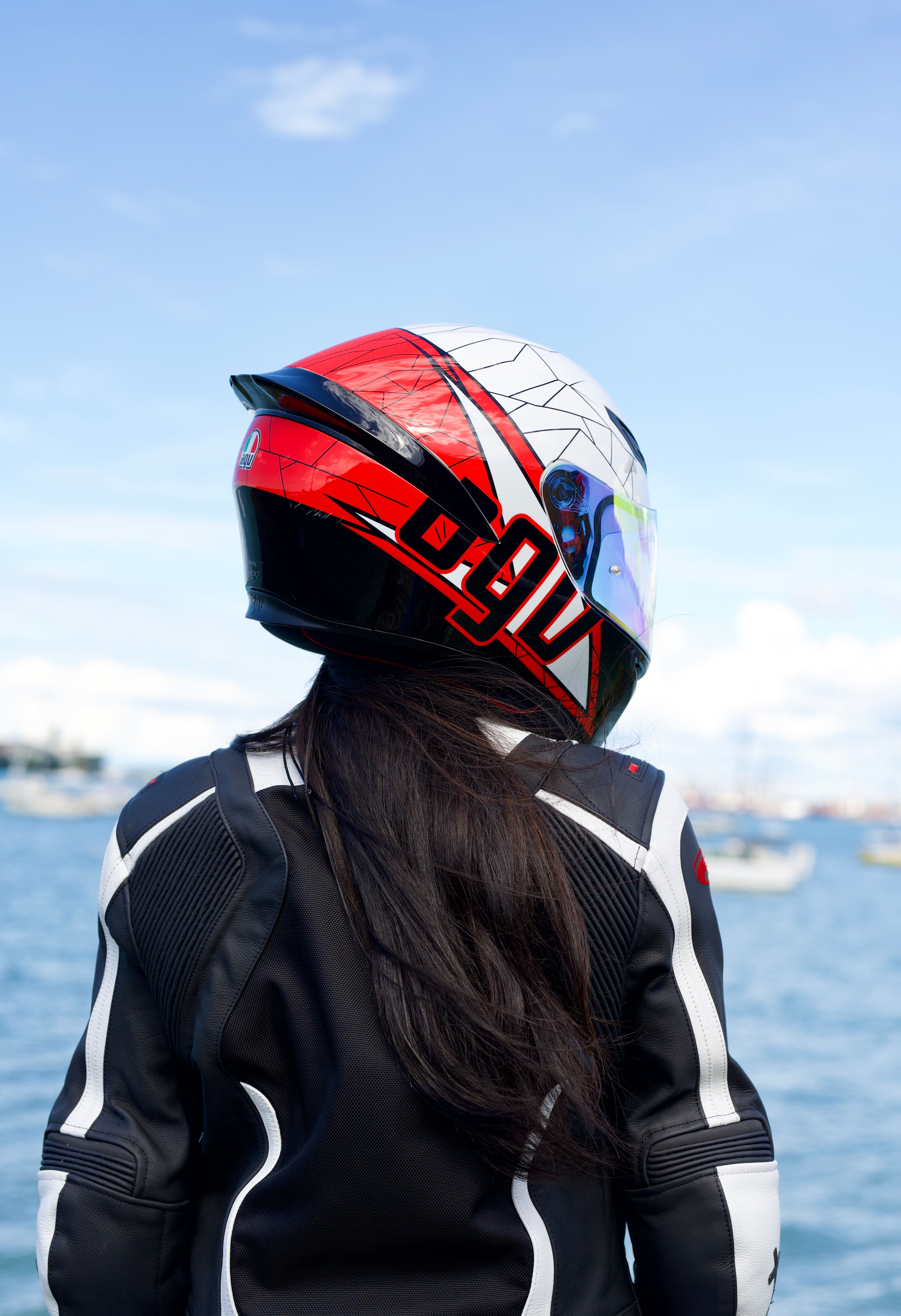 Rear view of a motorcyclist wearing a helmet by the water on a clear day.