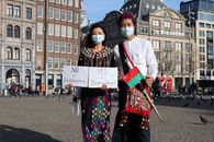 Two masked individuals in traditional attire protest for democracy in Amsterdam.