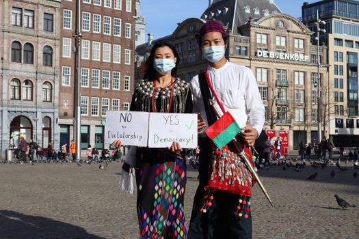 Two masked individuals in traditional attire protest for democracy in Amsterdam.