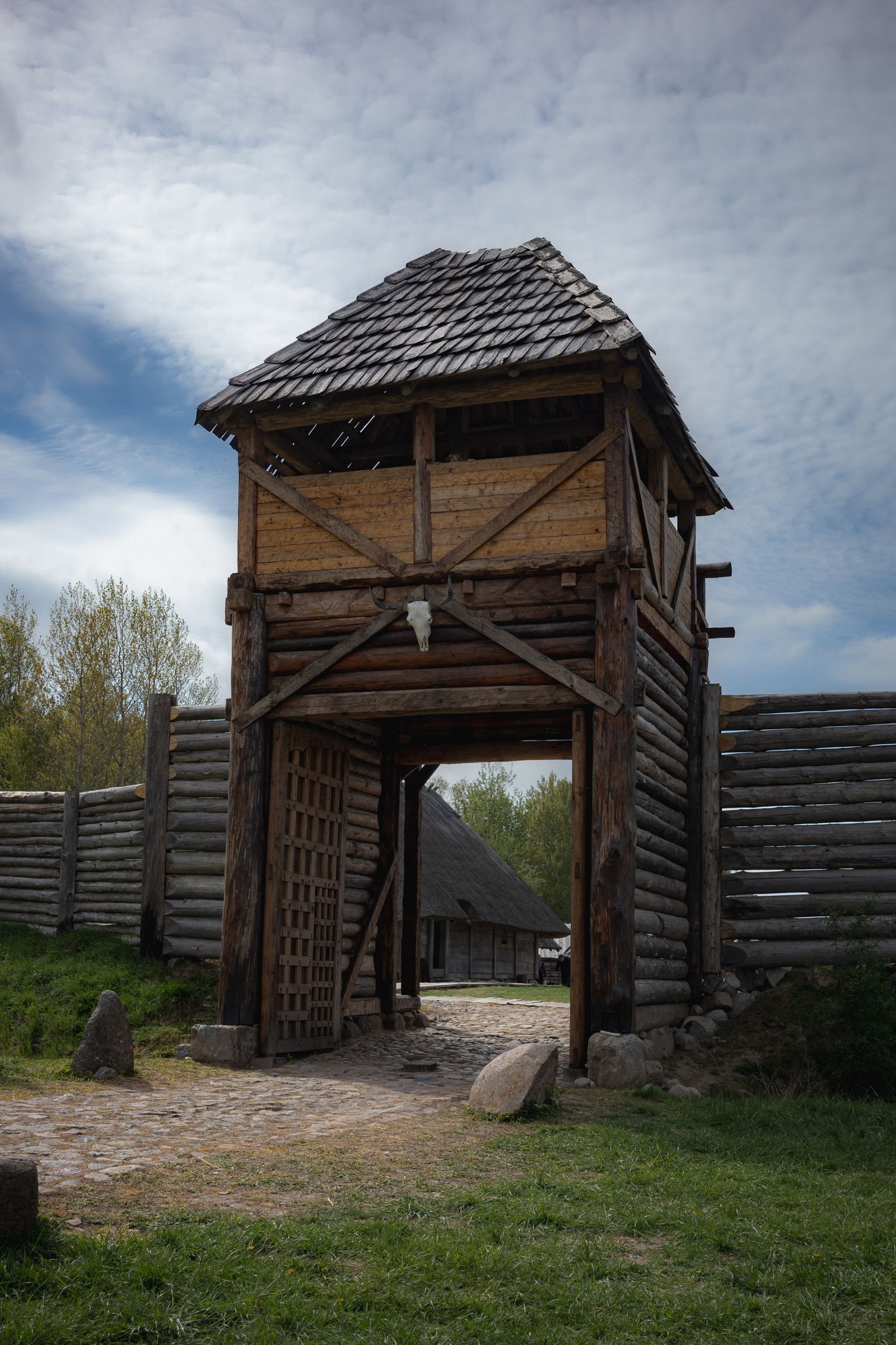 A timber watchtower above a wooden palisade wall under a bright sky, the gateway standing open beneath it