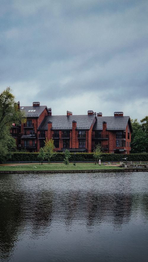 Free Stunning view of a red brick building surrounded by greenery and a serene lake. Stock Photo