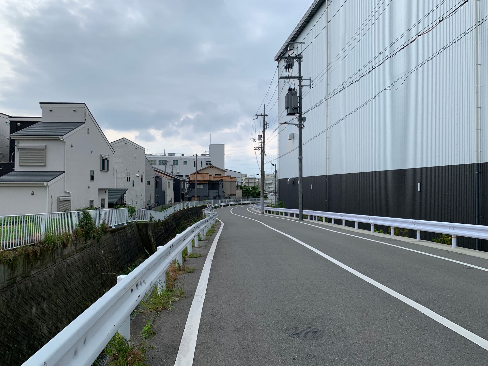 Curving urban street lined with industrial buildings and power lines under an overcast sky.