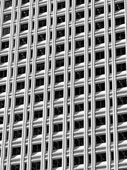 Black and white photo of a skyscraper facade featuring repetitive geometric patterns and windows.