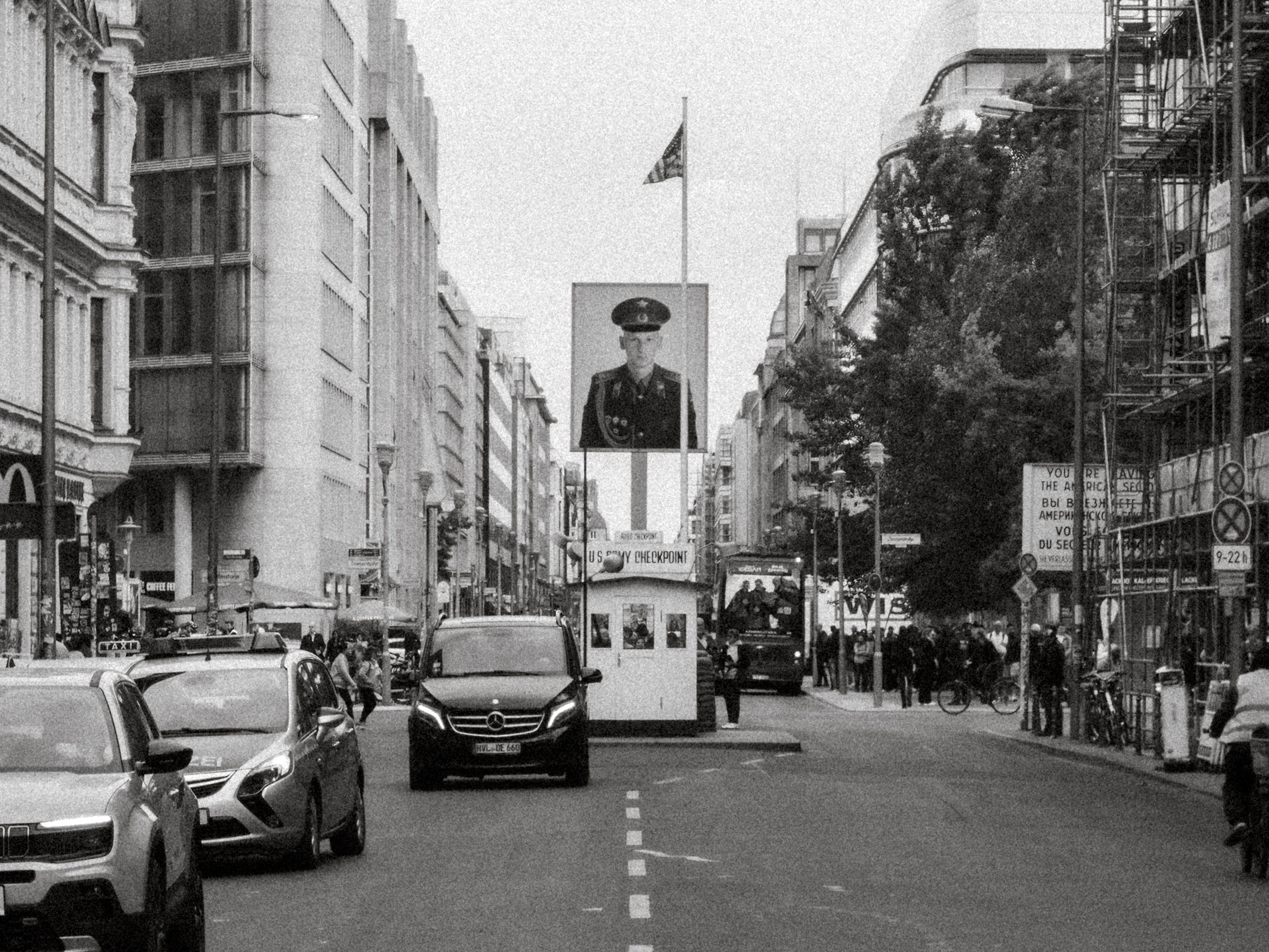 Black and white view of Checkpoint Charlie in Berlin with traffic and pedestrians.