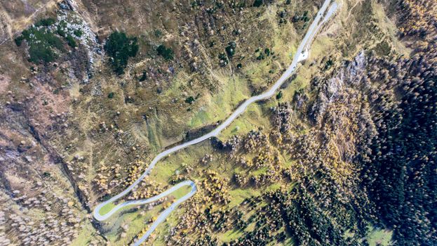 Aerial shot capturing a winding road through the rugged terrain and green landscape of Kärnten, Austria.