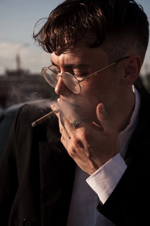 Free A man in glasses and suit smokes a cigarette outdoors during sunset. Stock Photo