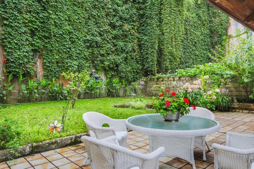 Free A charming garden patio with white wicker furniture surrounded by lush greenery and climbing vines. Stock Photo