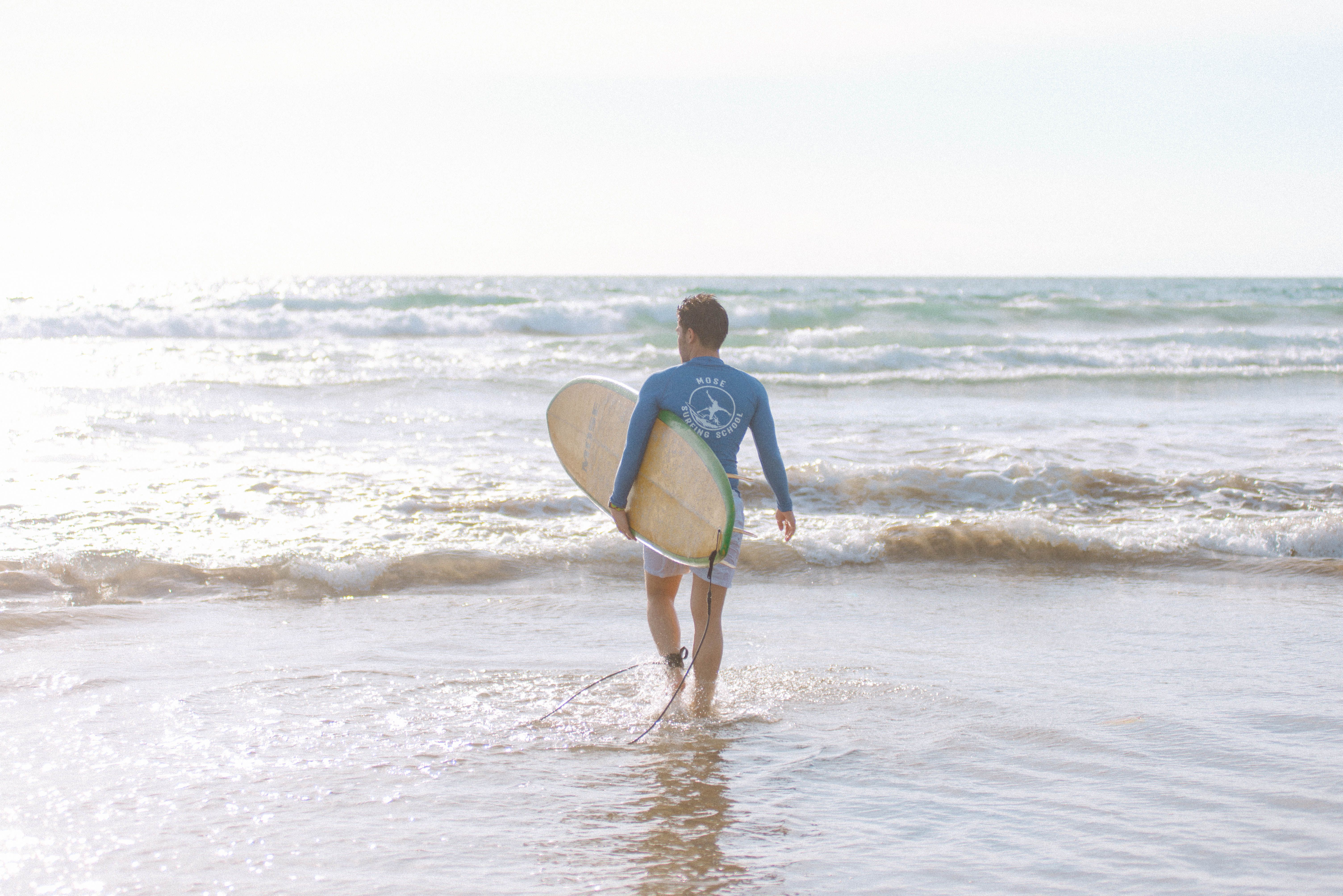 A surfer in Bali, Indonesia, enters the ocean carrying a surfboard, ready to catch waves.