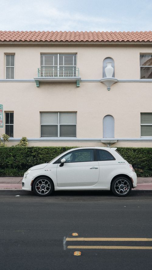 Free A stylish white car parked on a city street in front of a beige building. Modern urban lifestyle scene. Stock Photo