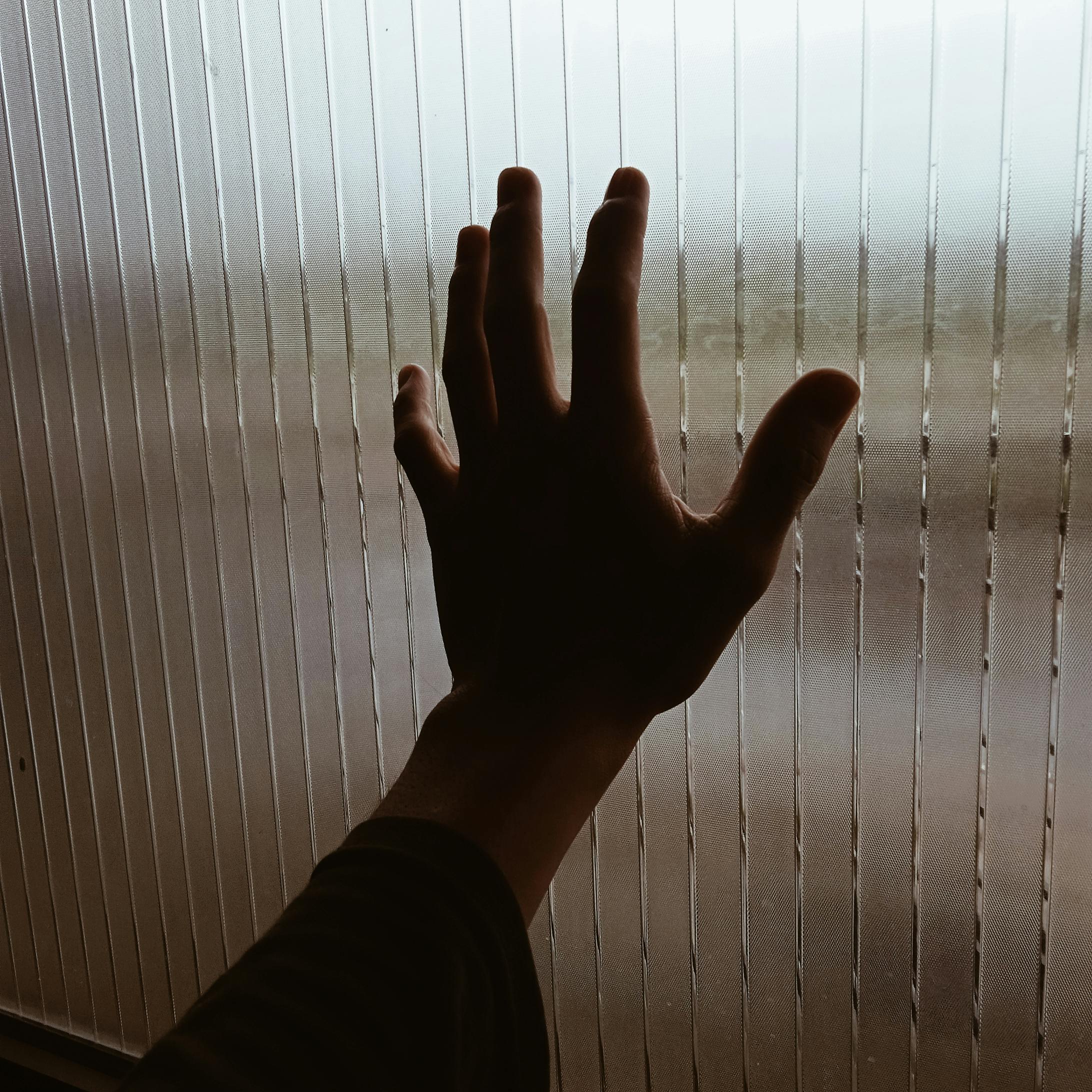 A silhouette of a hand gently pressing against a textured glass window, creating a moody ambiance.