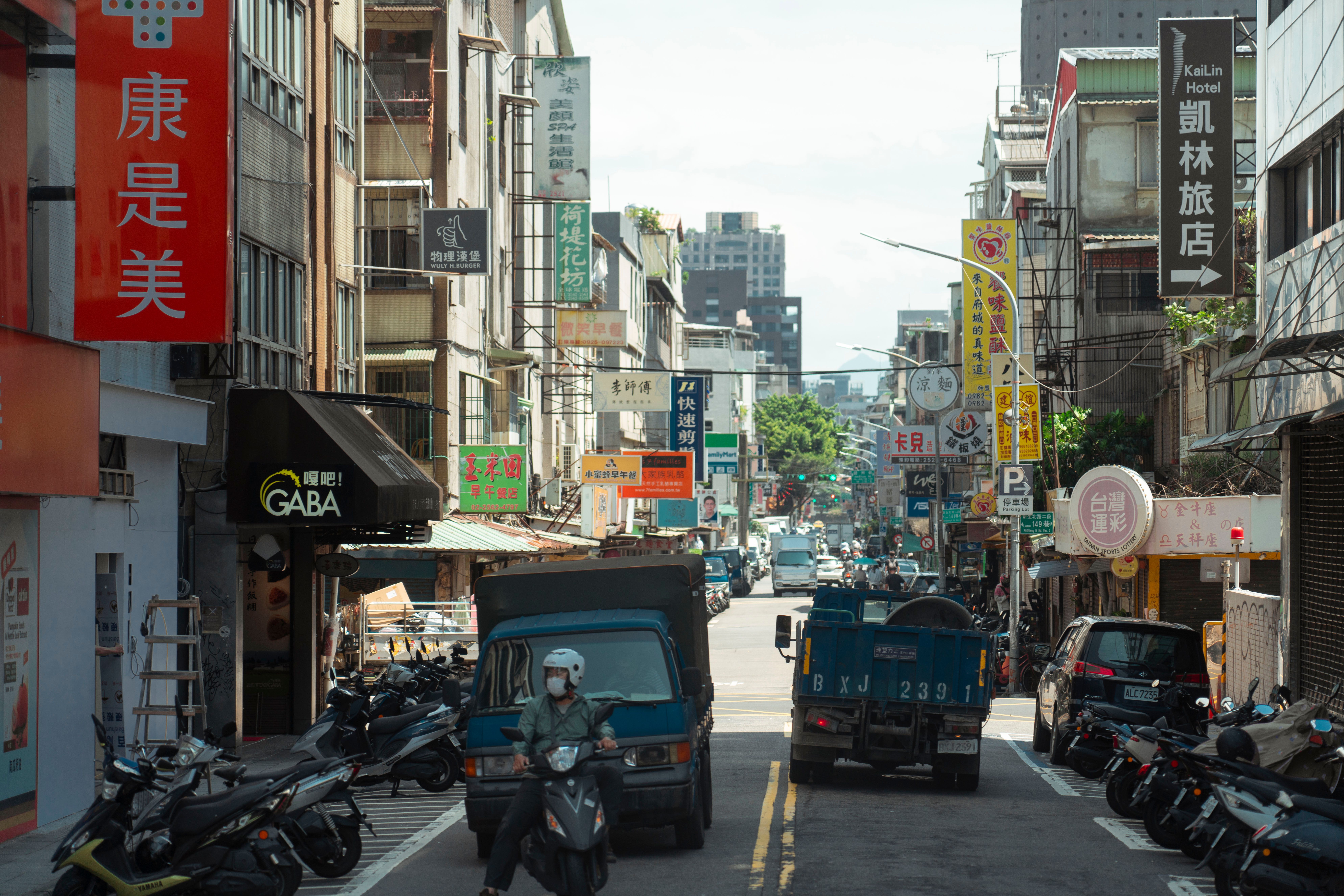 Vibrant Taipei street scene with scooters and cars amidst colorful shop signs.