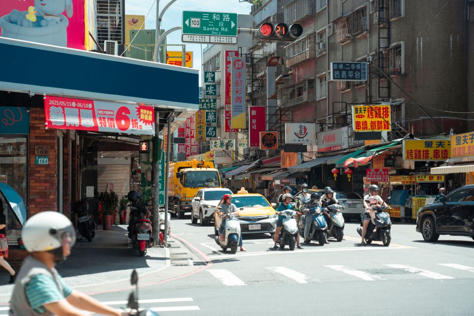 Bustling Taipei street scene with scooters, cars, and vibrant signage under a blue sky.
