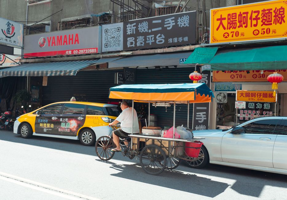 A street vendor pedals his food cart past shops in sunny Taipei City, Taiwan.