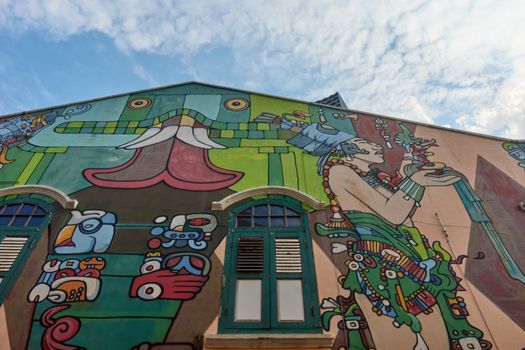Colorful mural featuring indigenous motifs on a building facade under a blue sky.