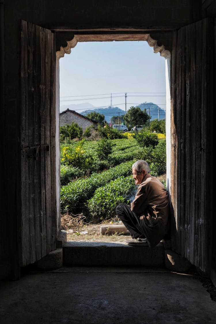 Senior Man Sitting At Outbuilding Entrance