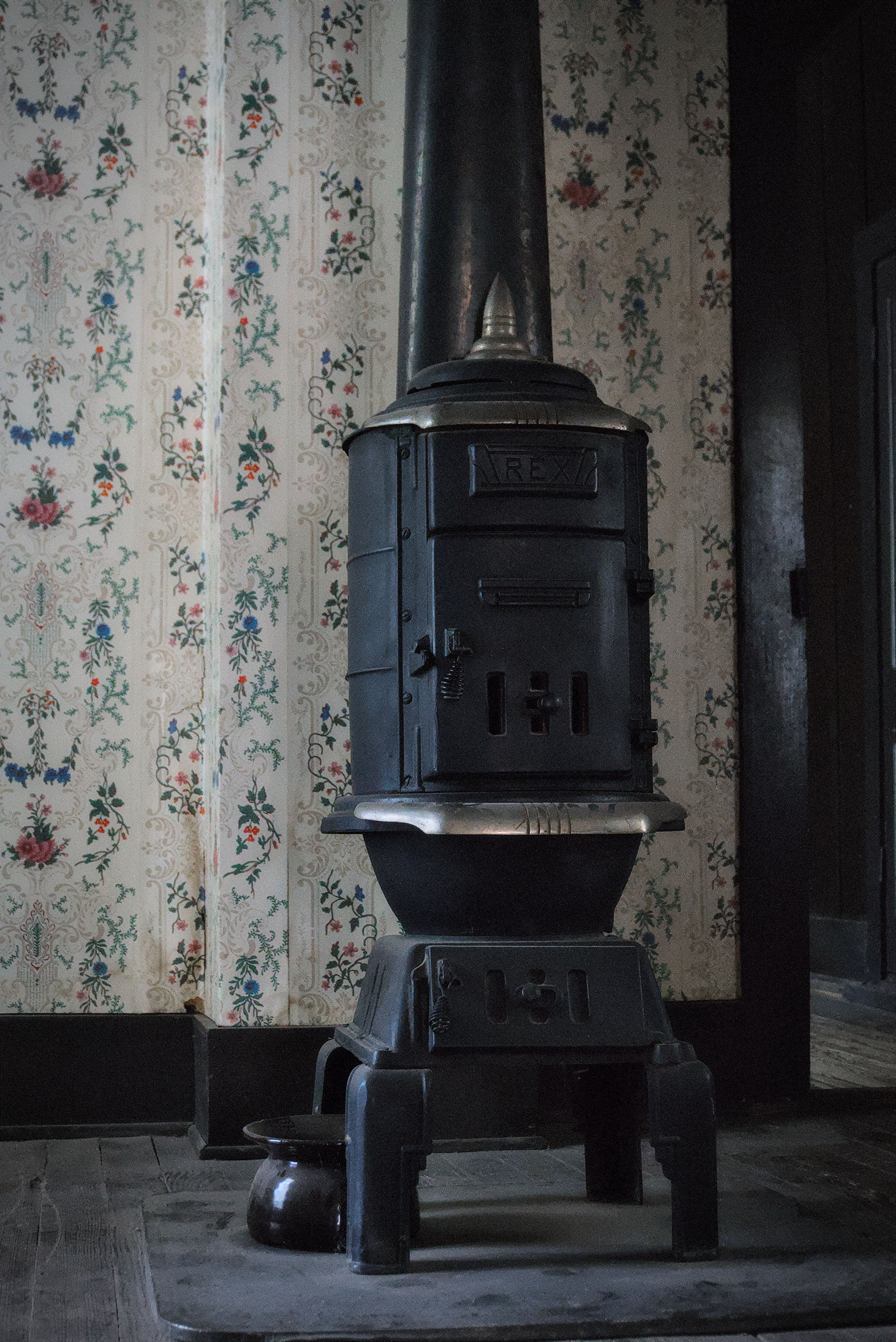 Vintage cast iron stove with floral wallpaper creates a rustic atmosphere.