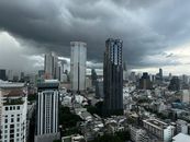 High-angle view of Bangkok's skyline with storm clouds gathering overhead, adding a dramatic touch.