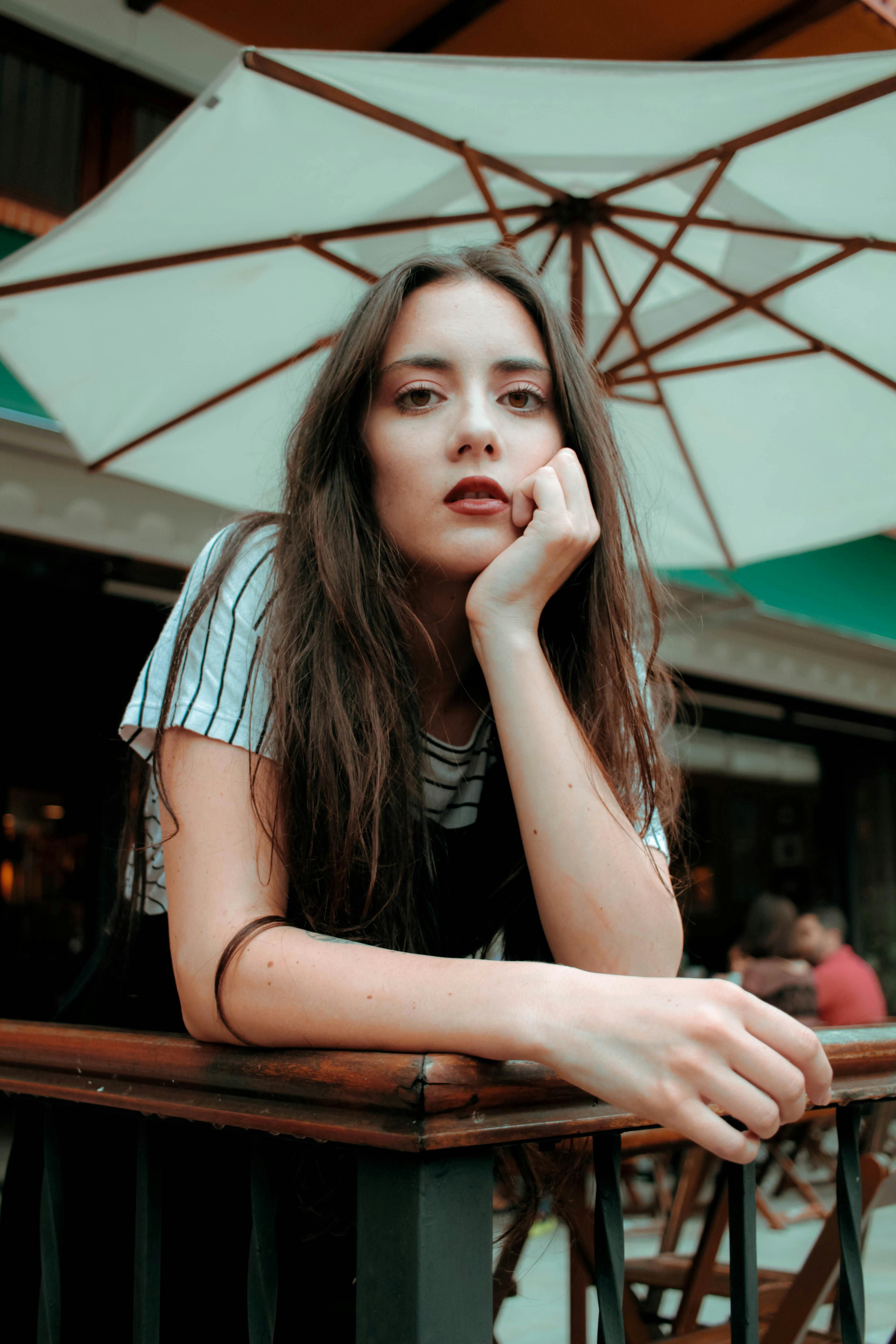 一名年轻女子留着长发，在户外遮阳伞下若有所思地摆着姿势